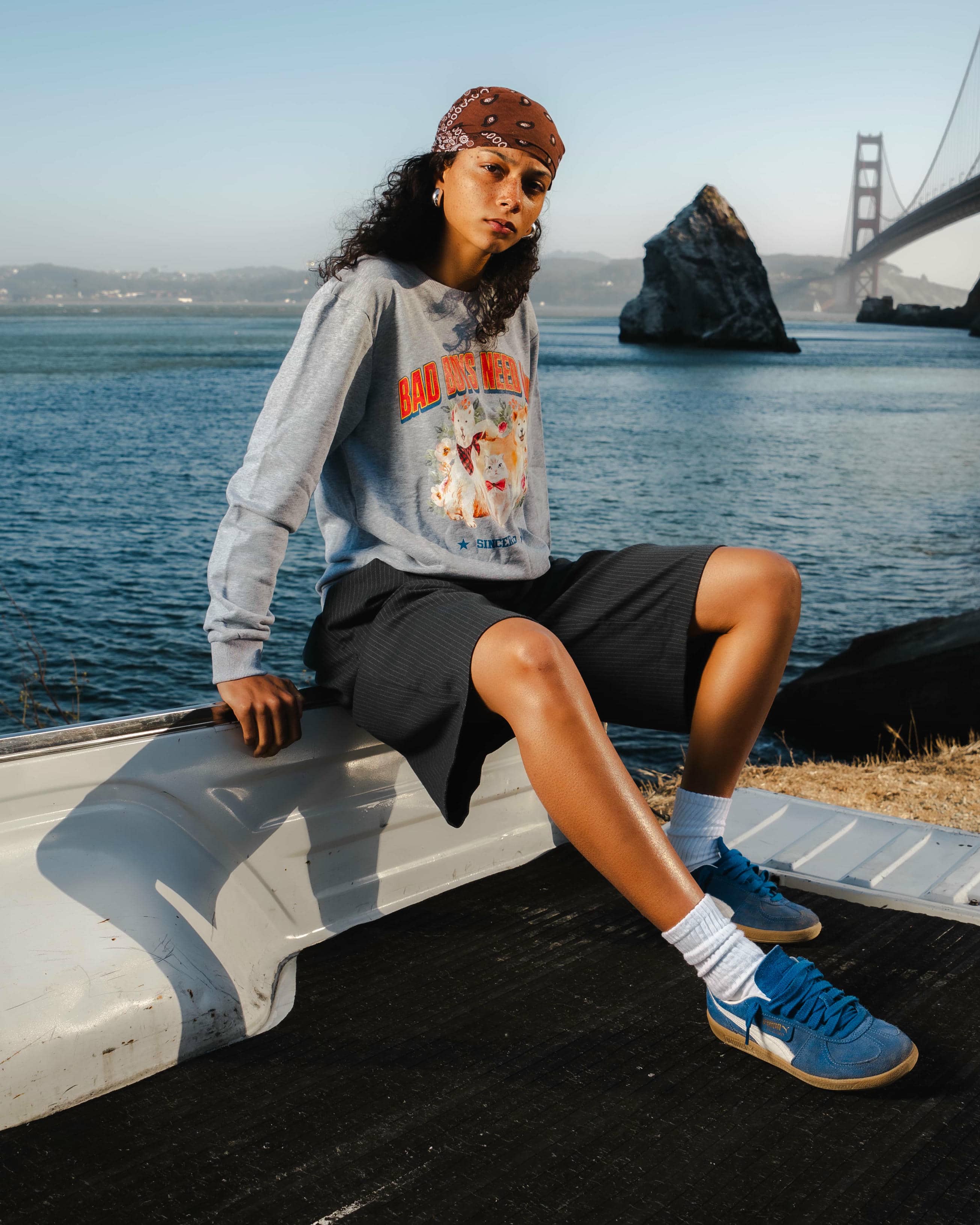 Person sitting on a railing by a body of water with a bridge in the background